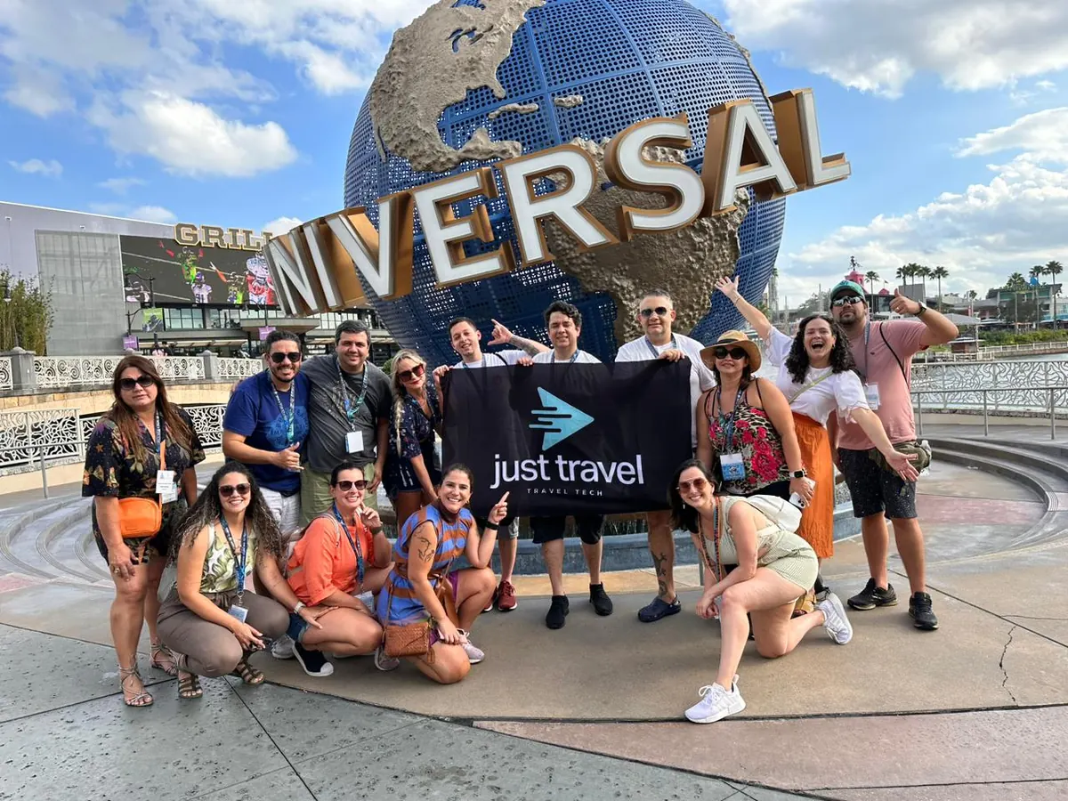 Equipe da Just Travel reunida com a bandeira da empresa em frente ao globo do Universal Studios, em Orlando